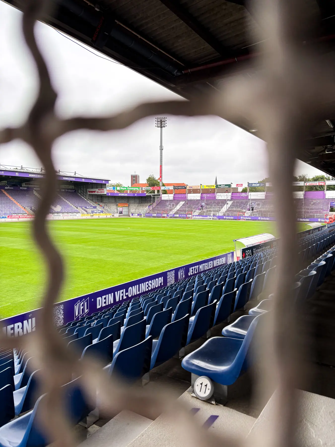 Stadion-Bremer-Bruecke-Begehung-01 Stadion Bremer Brücke: Blick auf das Fußballfeld und die Tribüne mit blauen Sitzen.