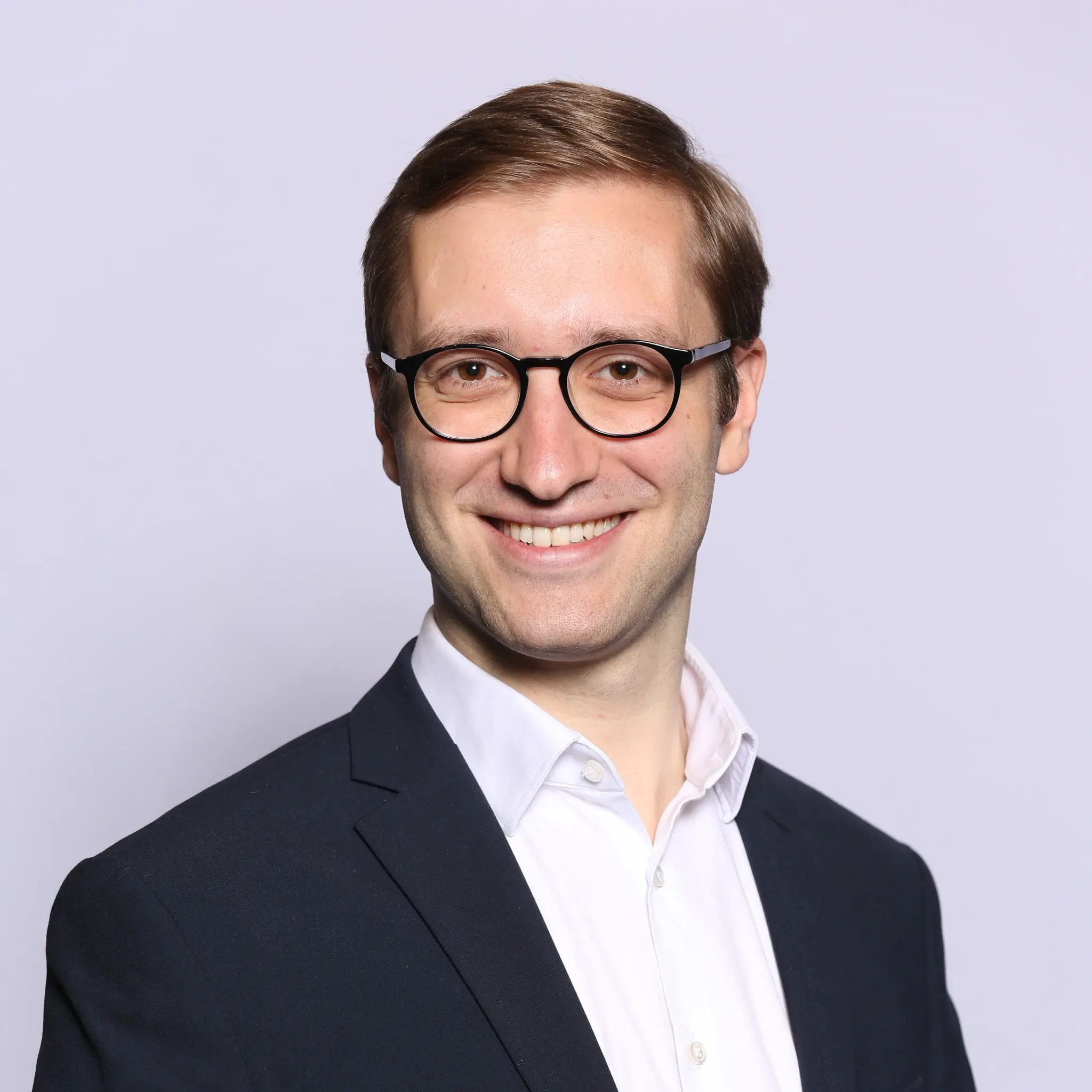 Porträt von Joshua Hofer mit Brille und Anzug, lächelnd.